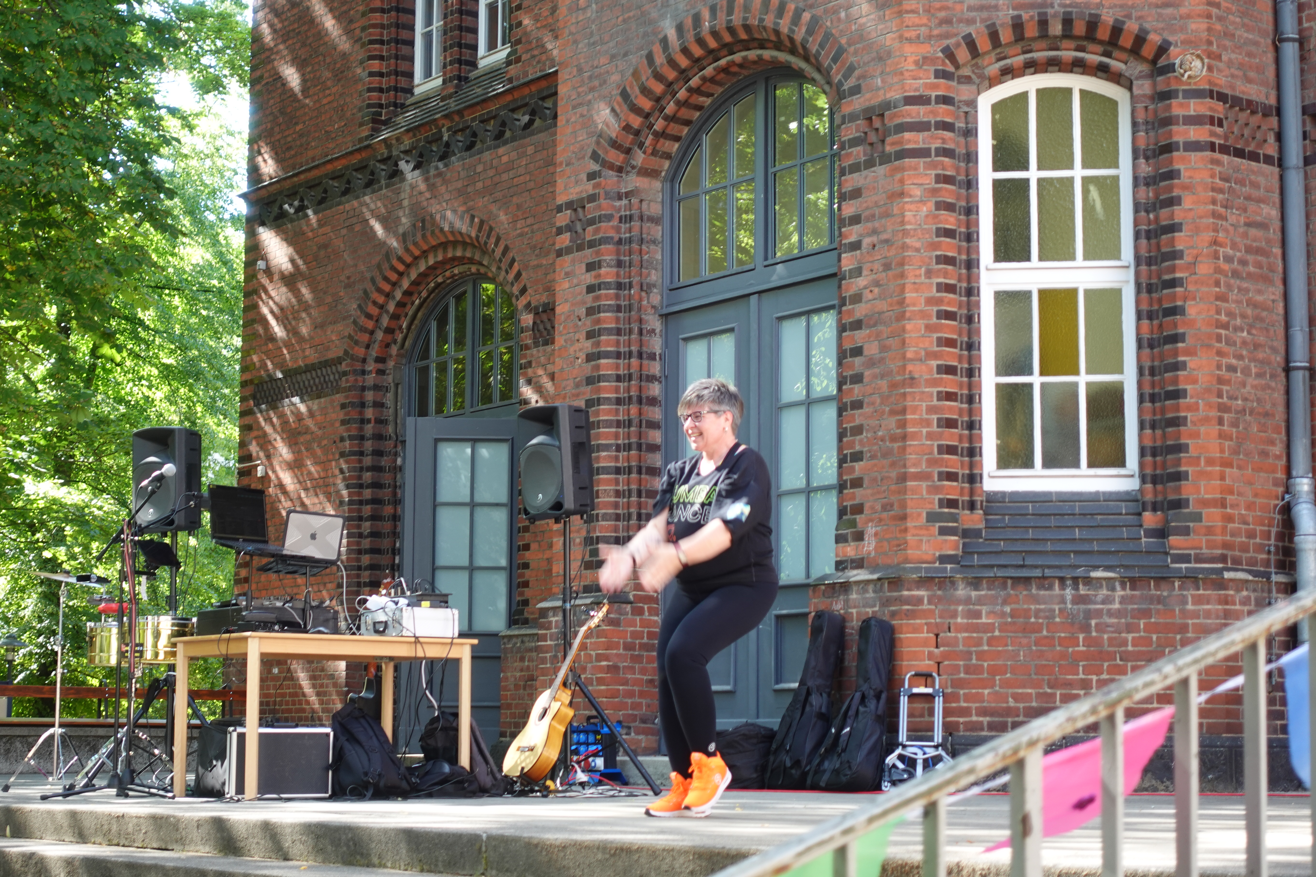 Eine Frau tanzt Zumba. Im Hintergrund sieht man ein Backsteingebäude.