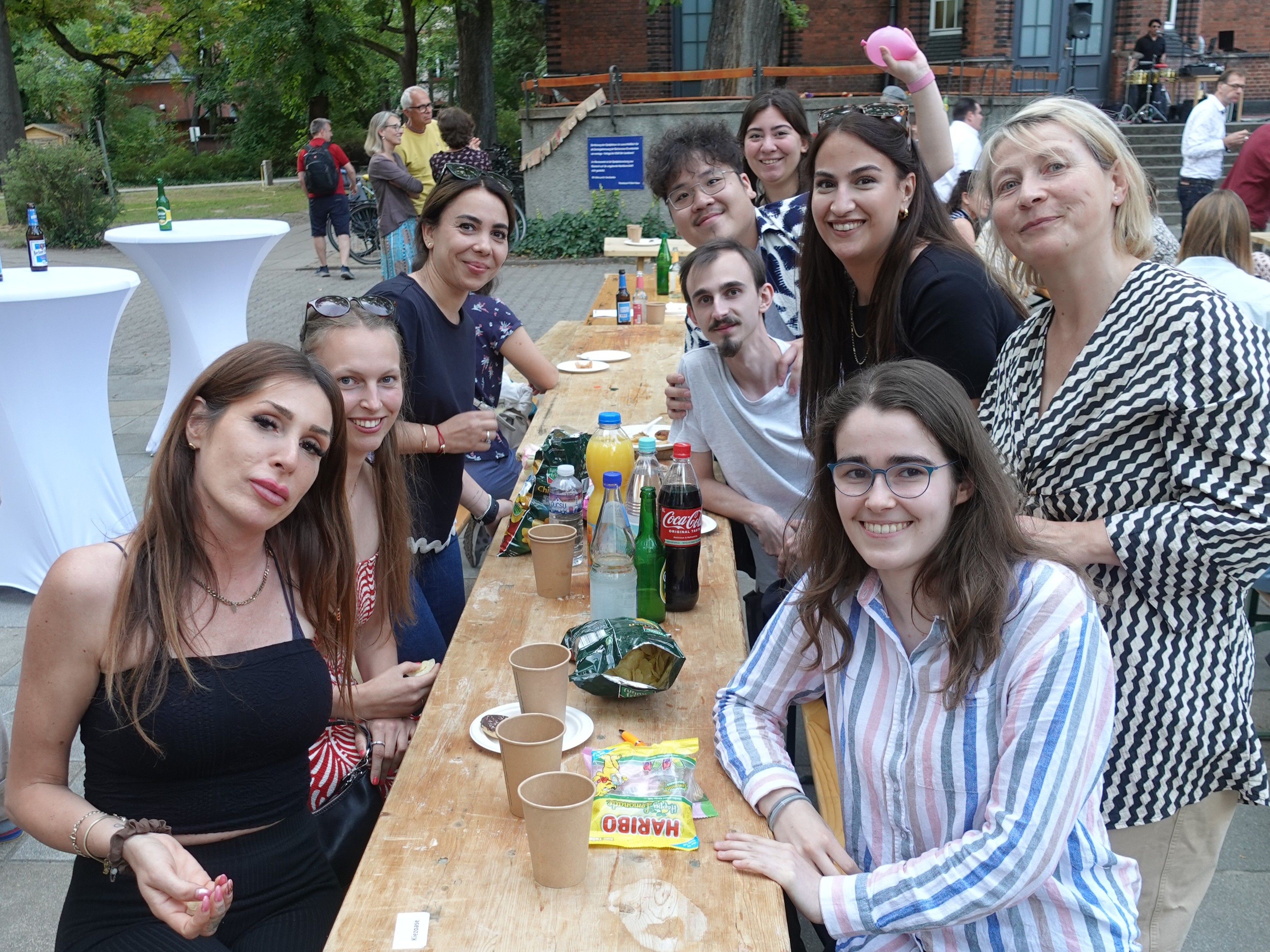 Neun erwachsene Personen sitzen an einer Festzeltgarnitur und lächeln in die Kamera. Auf dem Tisch stehen Getränke.
