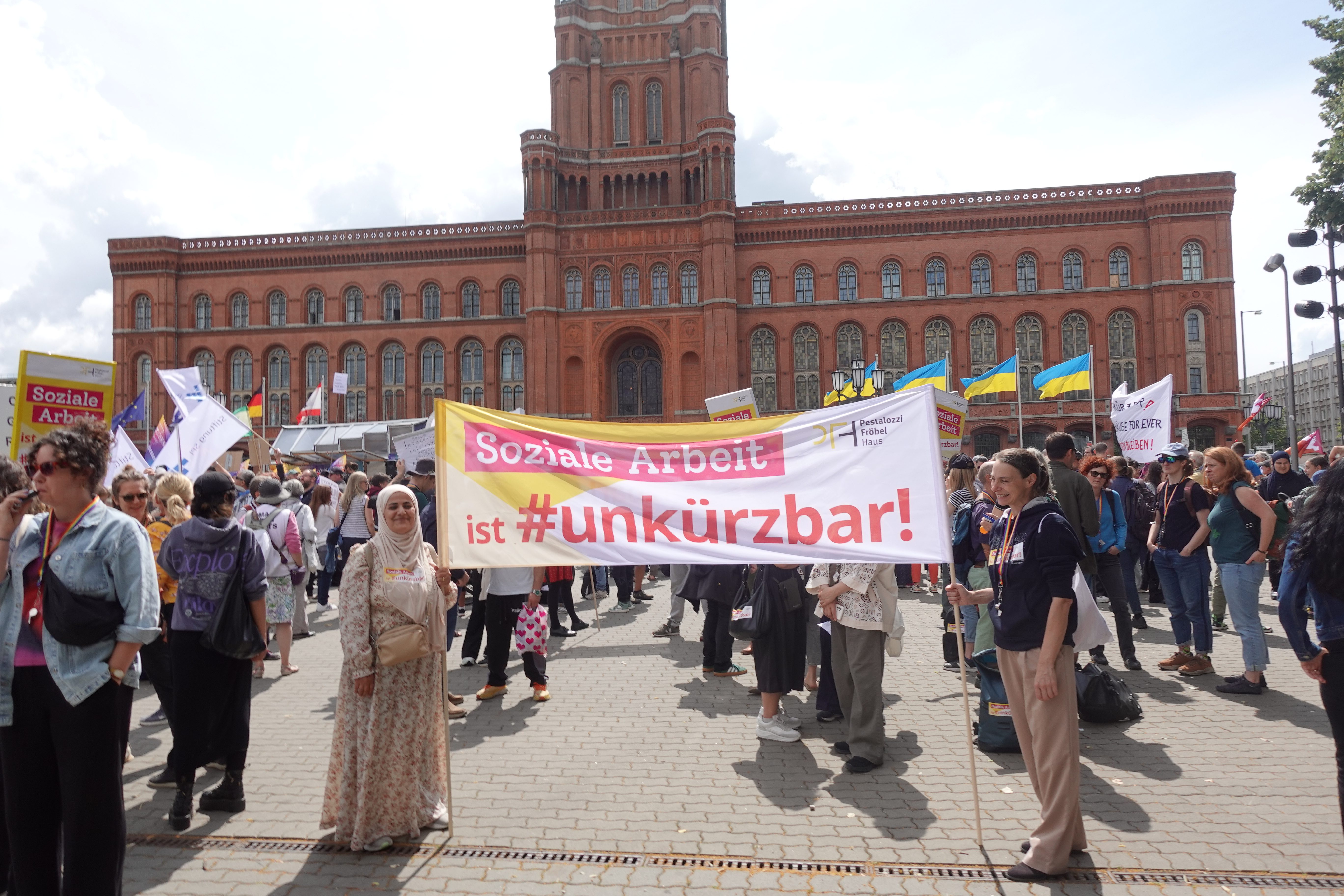 Soziale Arbeit ist #unkürzbar! Mitarbeiter*innen des PFH demonstrieren vor dem Roten Rathaus mit Schildern.