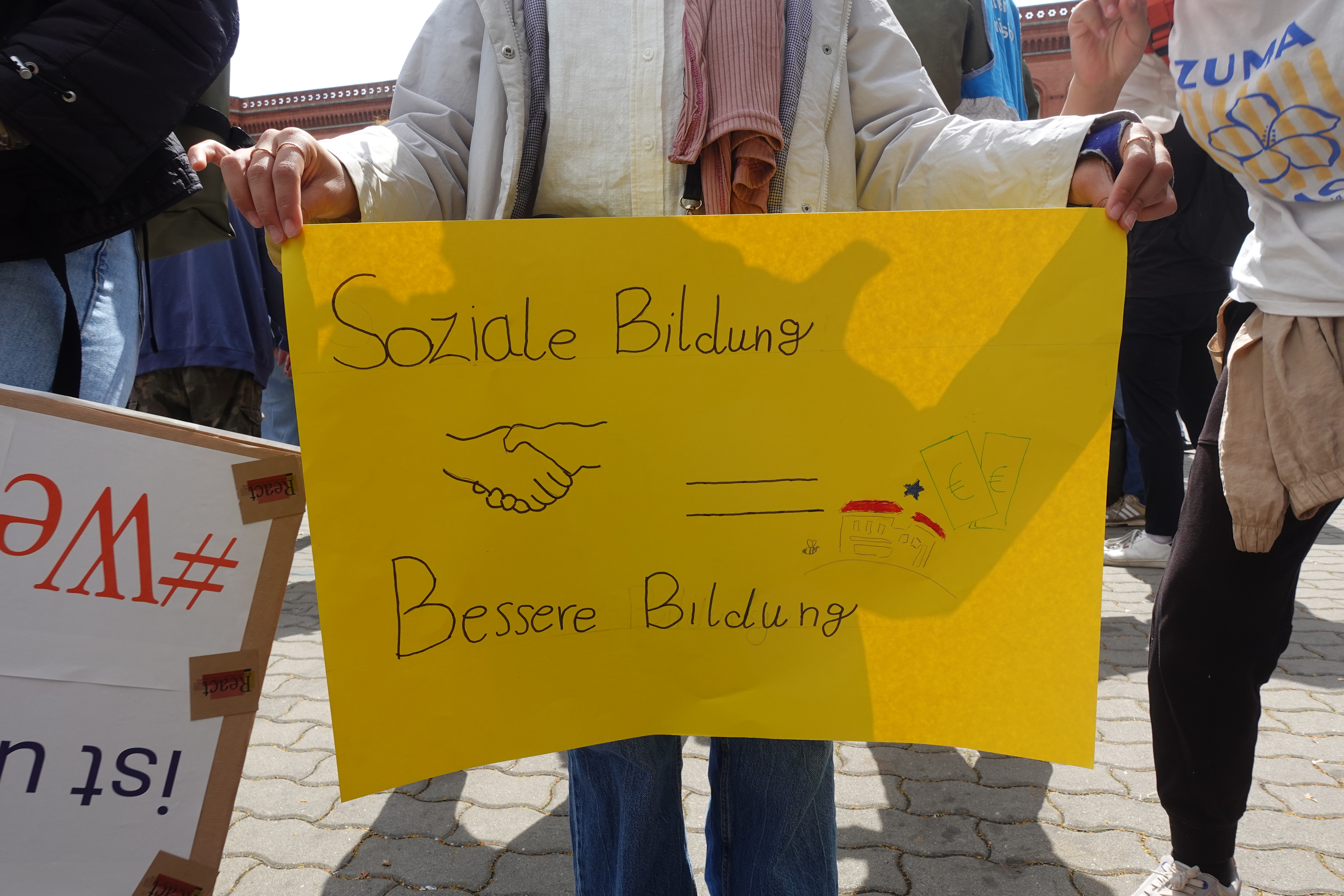 Kind hält ein gelbes Plakat: Soziale Bildung = Besser Bildung. 
