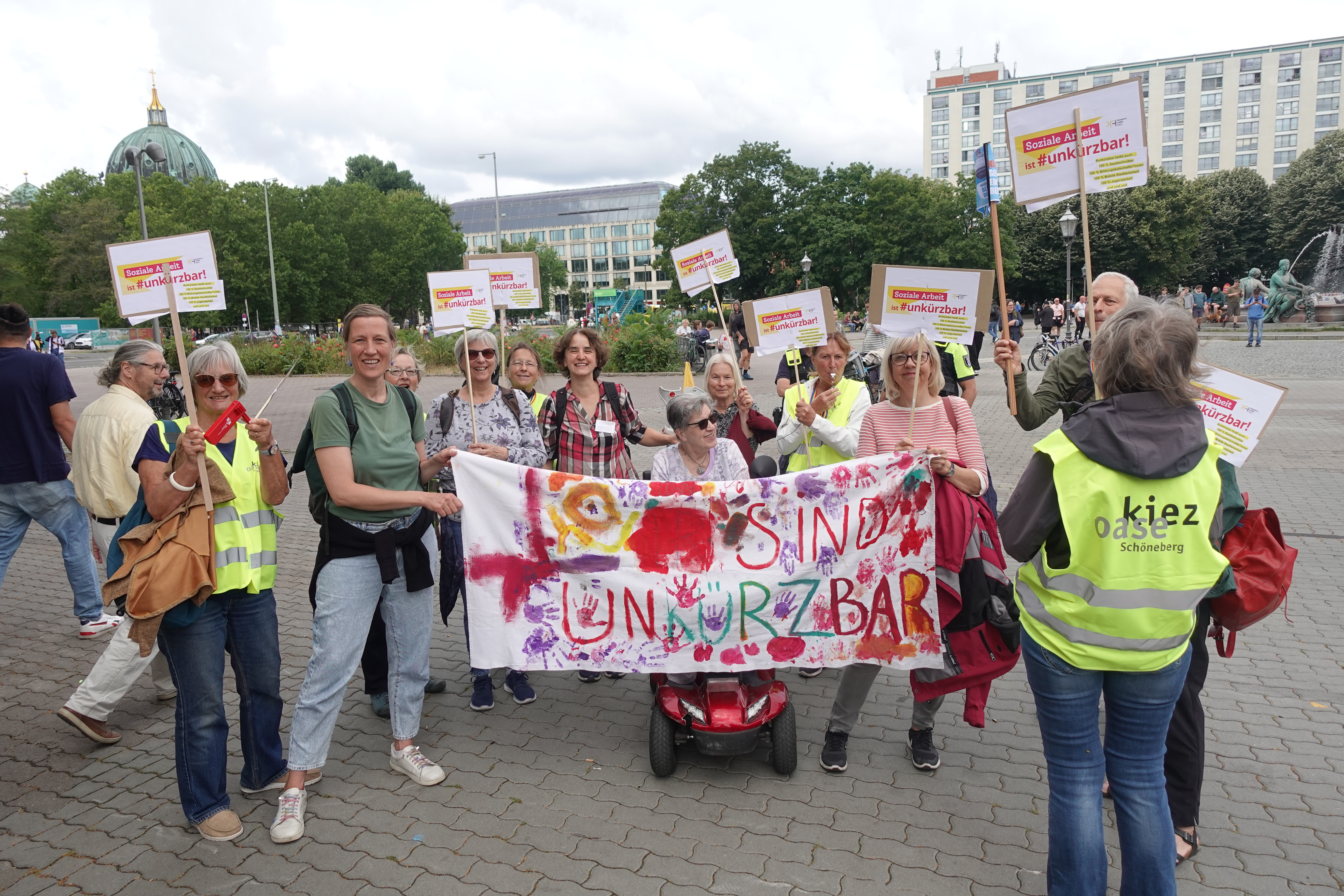 Soziale Arbeit ist #unkürzbar! Mitarbeiter*innen des PFH (Kiezoase) demonstrieren vor dem Roten Rathaus mit Schildern.