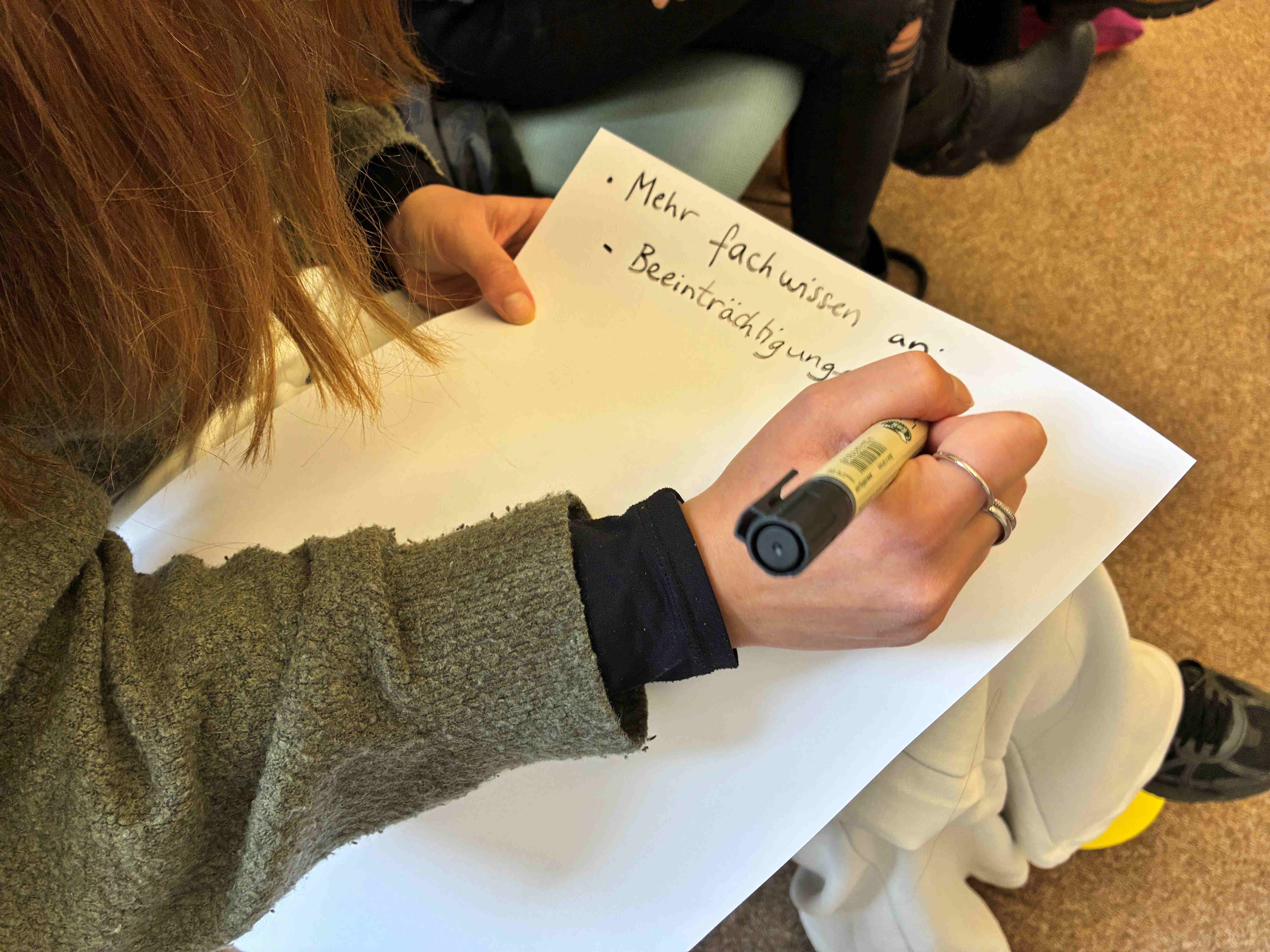 Eine Person schreibt auf ein Blatt Papier, das auf ihrem Schoß liegt.