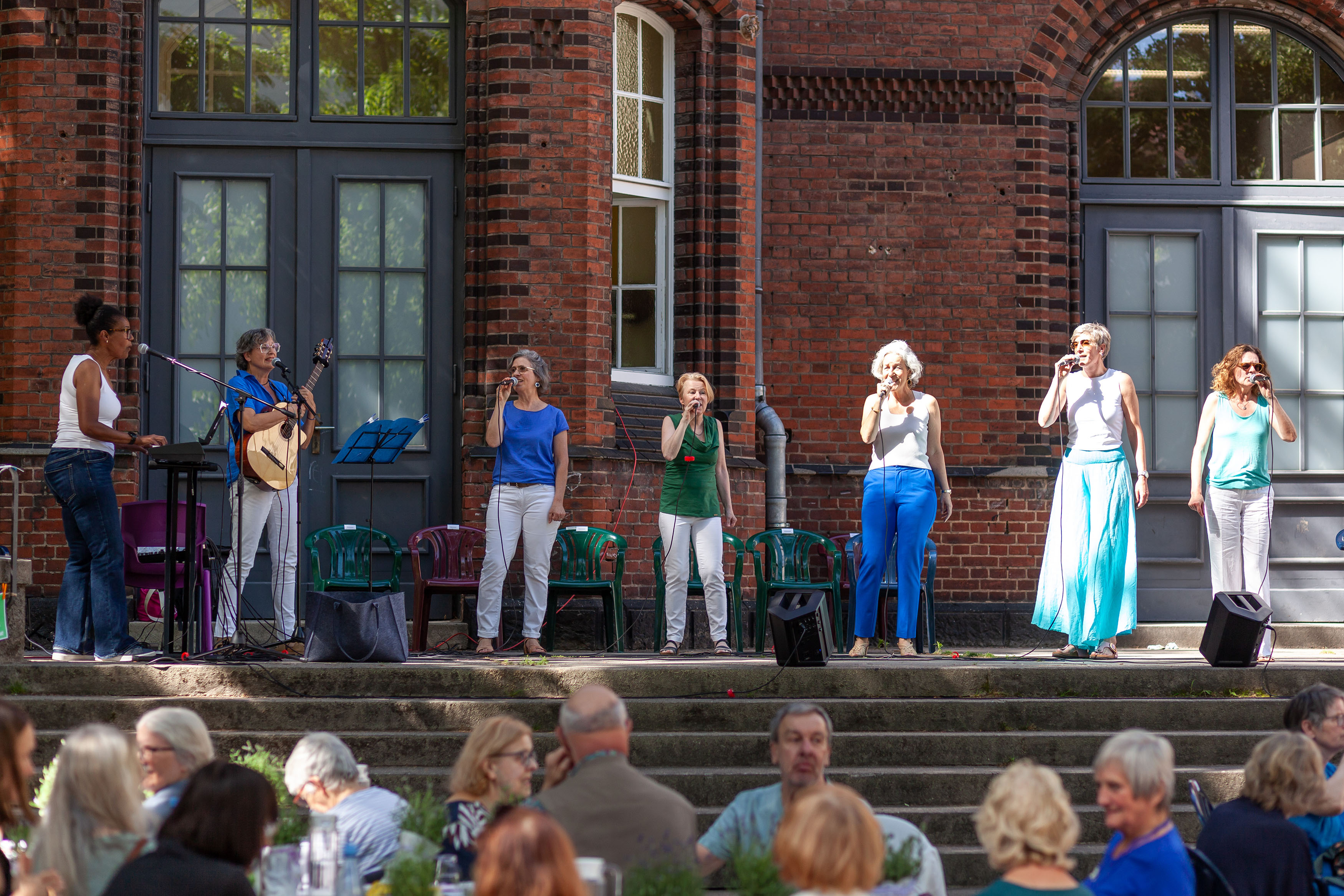 Der Chor steht auf der Bühne. Es sind 7 Frauen, eine am Keyboard, eine an der Gitarre, die anderen halten ein Mikro in der Hand. Sie singen mehrstimmige sommerlich stimmungsvolle südamerikanische Klassiker.