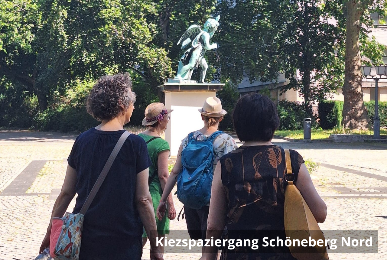 Kiezspaziergang Schöneberg Nord: Vier Personen laufen über einen gepflasterten Platz. Im Hintergrund ist eine Statue und grüne Bäume.