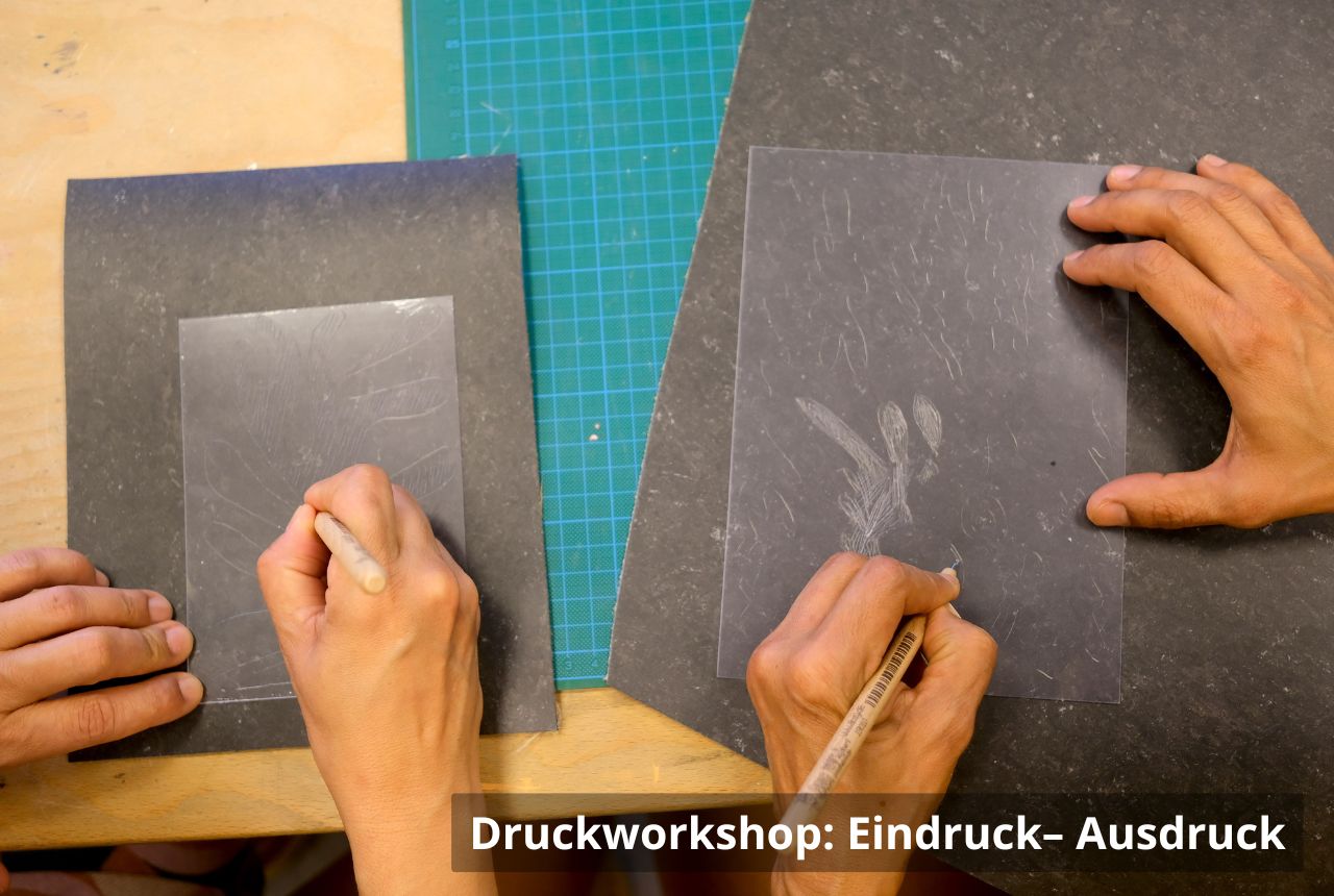 Zwei Personen zeichnen mit Bleistift auf dunkle Platten. Die Platten liegen auf dunklen Unterlagen neben einer grünen Schneidematte; nur die Hände sind zu sehen.