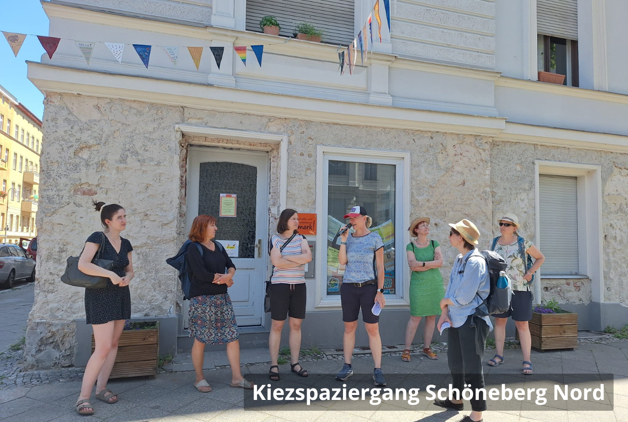 Kiezspaziergang Schöneberg Nord: Sieben Personen stehen auf dem Fußweg vor einem Haus mit bunter Wimpelkette. Eine Frau spricht in ein Mikrofon.