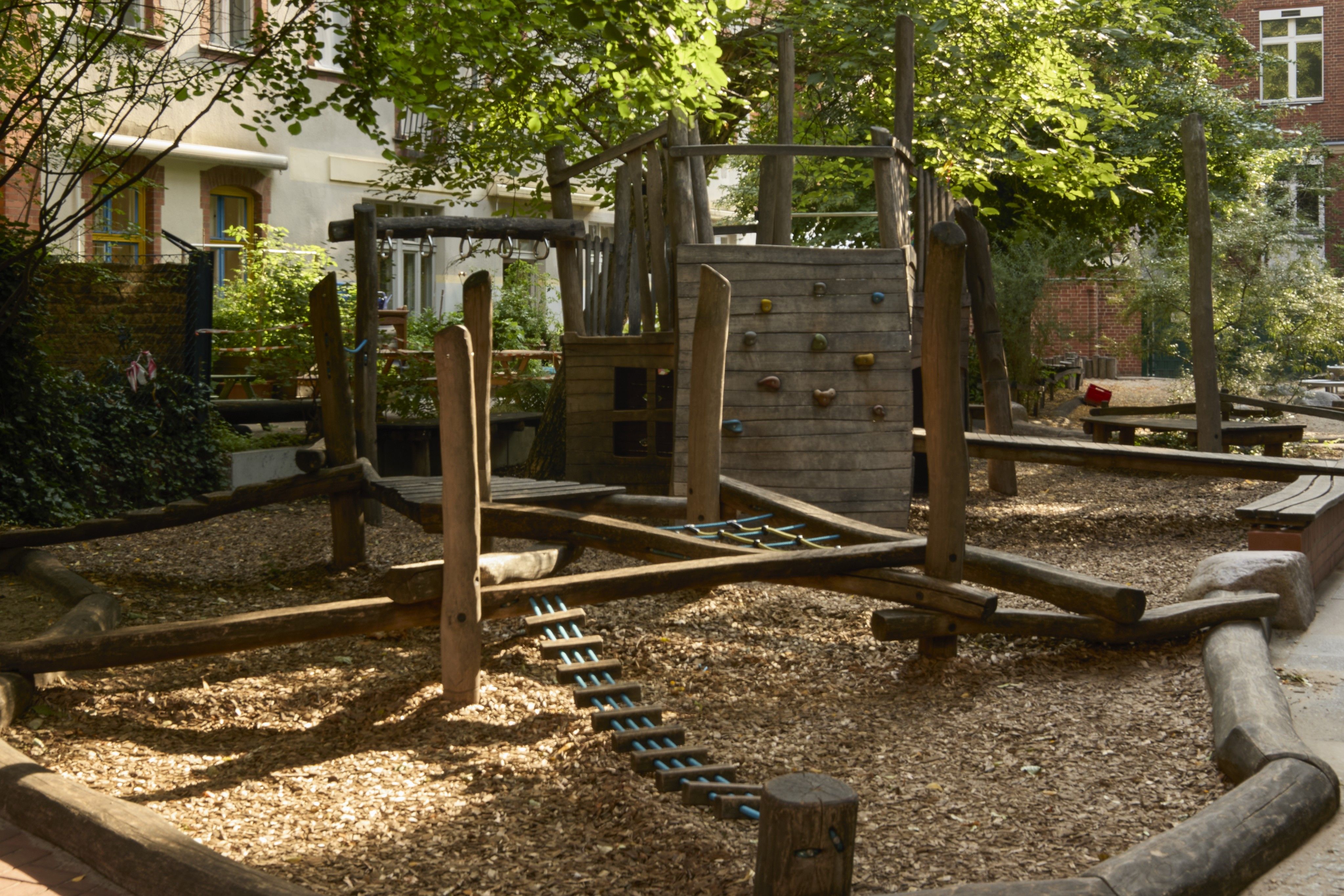 Schattiger Spielplatz aus Holz unter einem großen Baum.