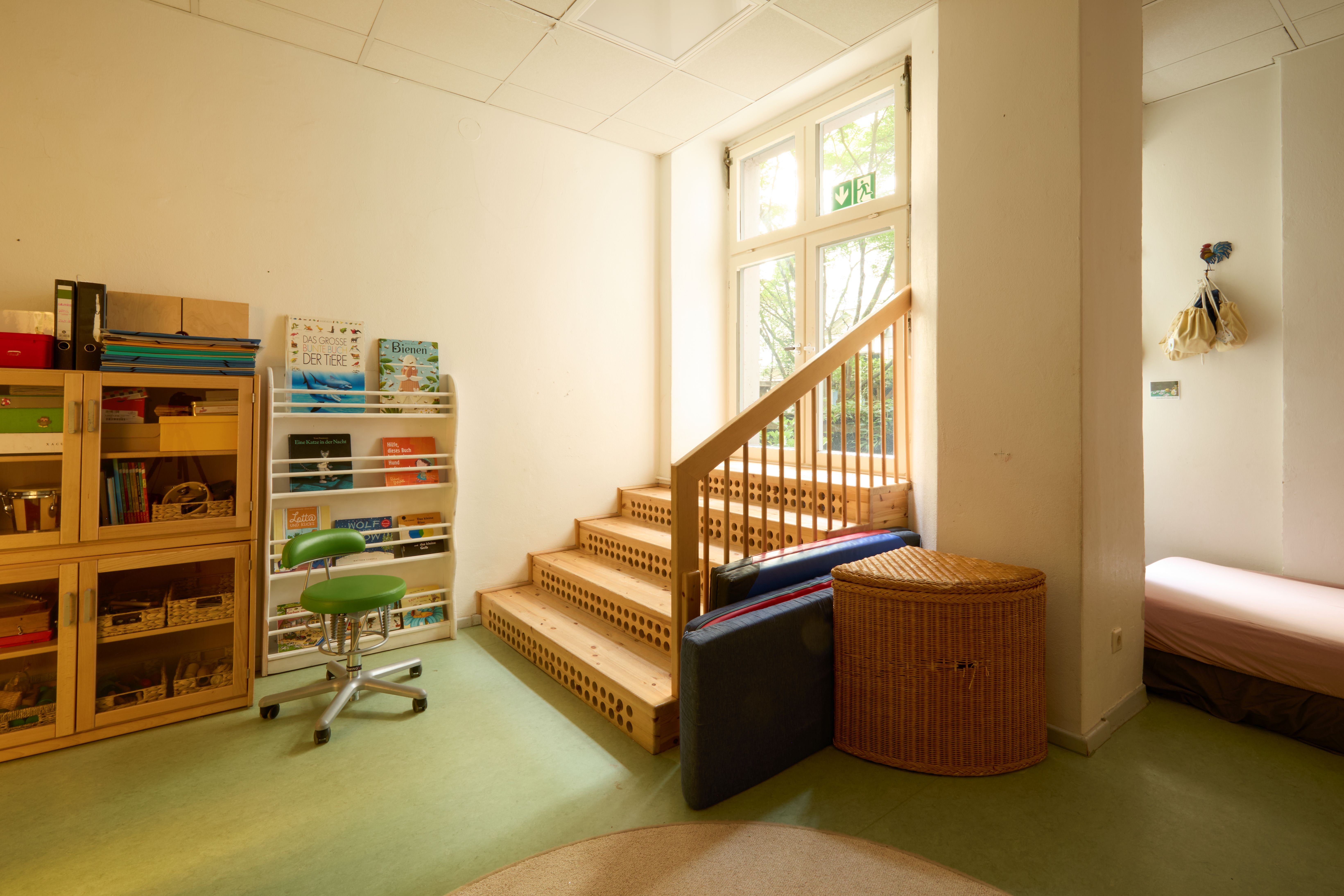 Heller Innenbereich mit breiter Holztreppe, daneben Bücherregal mit Kinderbüchern.