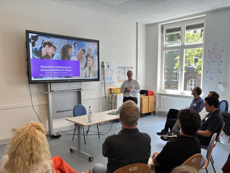 Dr. Marlies Kroetsch hält einen Vortrag. Im Hintergrund sieht man eine Präsentation. Im Vordergrund sitzen ca. 10 Personen und hören aufmerksam zu.