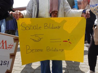 Kind hält ein gelbes Plakat: Soziale Bildung = Besser Bildung. 