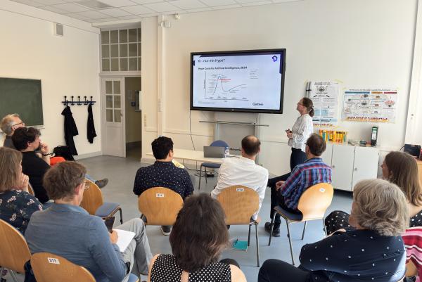 Dr. Marlies Kroetsch hält einen Vortrag. Im Hintergrund sieht man eine Präsentation mit einer Grafik. Im Vordergrund sitzen ca. 15 Personen und hören aufmerksam zu. 