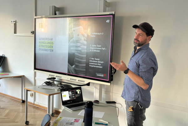 Ein Mann steht als Referent neben einer Präsentation und spricht.