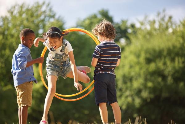 Zwei Kinder halten einen großen Ring in der Hand. Ein drittes Kind springt hindurch.