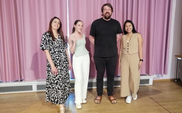 Vier Personen stehen nebeneinander. Sie lächeln in die Kamera. 