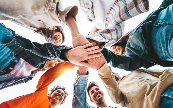 Junge Menschen bilden einen Kreis und legen die Hände übereinander